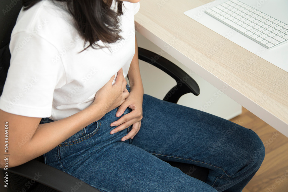 Abdominal pain in woman with stomachache illness from menstruation cramps. Woman sitting on a chair with stomach pain.