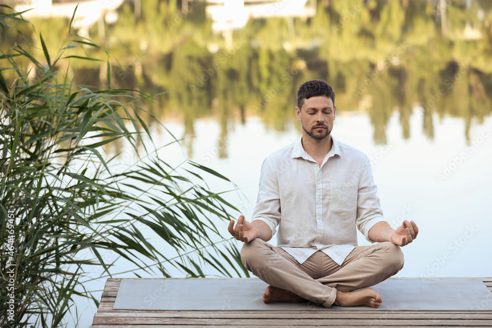 Man meditating on wooden pier near river. Space for text Man meditating on wooden pier near river. Space for text