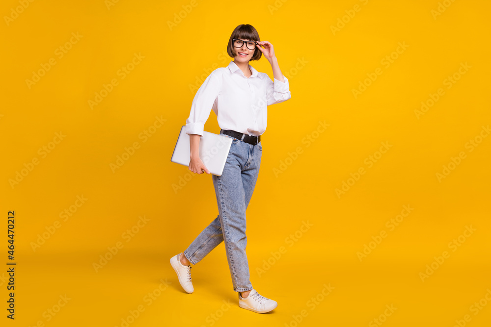 Photo of confident lady carry laptop go wear eyeglasses white shirt jeans sneakers isolated yellow color background Photo of confident lady carry laptop go wear eyeglasses white shirt jeans sneakers isolated yellow color background