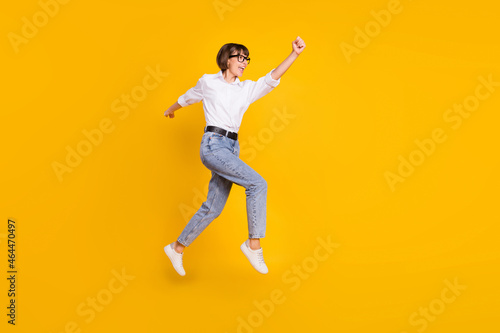 Profile photo of savior lady jump run raise fist wear eyewear white shirt jeans footwear isolated yellow color background