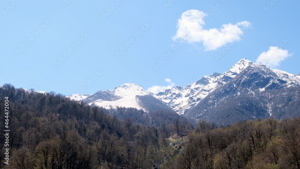 beautiful landscape of snow-capped mountains with white clouds on blue sky on a sunny day at Krasnaya Polyana in Sochi, Russia. Famous ski resort beautiful landscape of snow-capped mountains with white clouds on blue sky on a sunny day at Krasnaya Polyana in Sochi, Russia. Famous ski resort