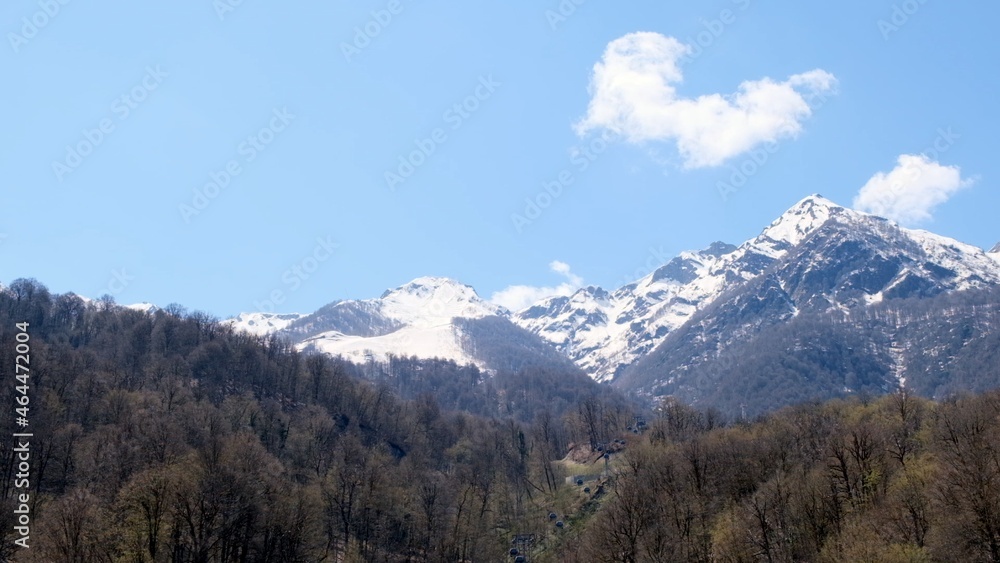 beautiful landscape of snow-capped mountains with white clouds on blue sky on a sunny day at Krasnaya Polyana in Sochi, Russia. Famous ski resort