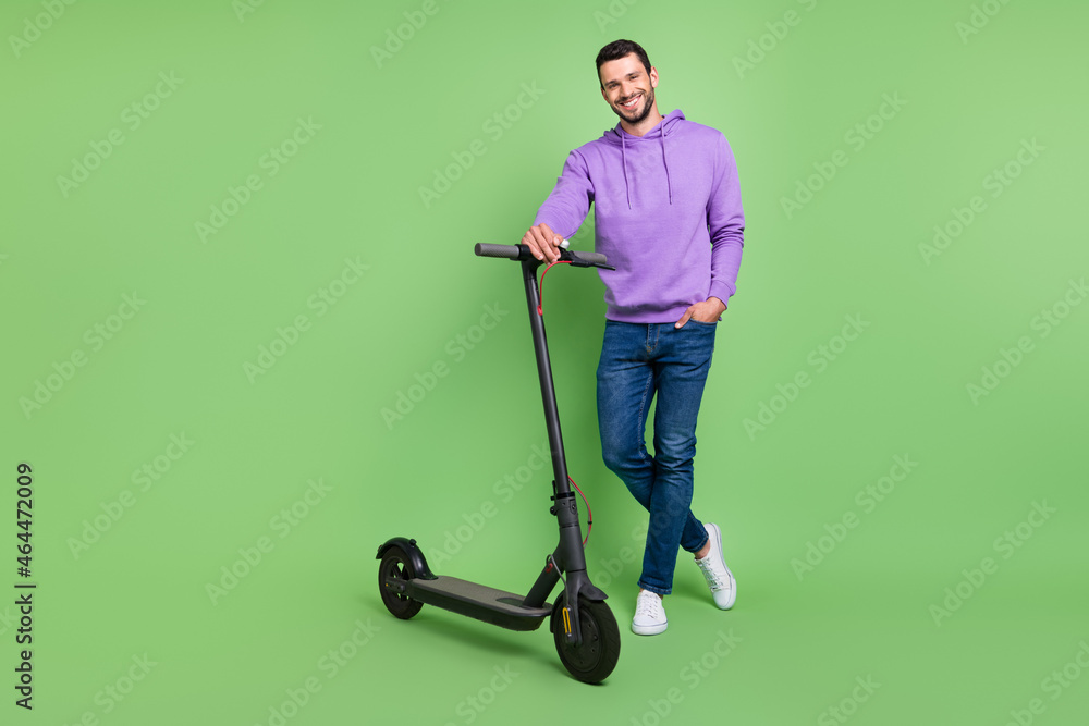 © deagreez - Full length photo of young cheerful man happy positive smile walk electric scooter isolated over green color background