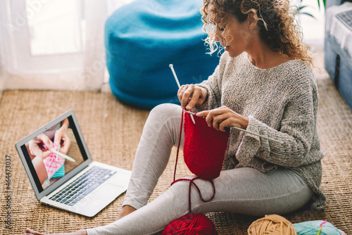 Young woman knitting wool using needle while watching online tutorial on laptop at home. Woman watching needlework lessons, a laptop and home hobbies. Caucasian woman learning to knit online photo