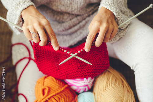 High angle view of hands of woman doing knitting work with needle, sitting on floor in living room at home. Close up woman hands with knitting needle and doing knit job.