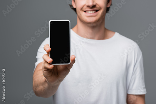 Cropped view of smartphone in hand of blurred smiling man isolated on grey