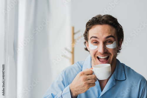 Cheerful man in eye patches and pajama holding cup of coffee at home © LIGHTFIELD STUDIOS