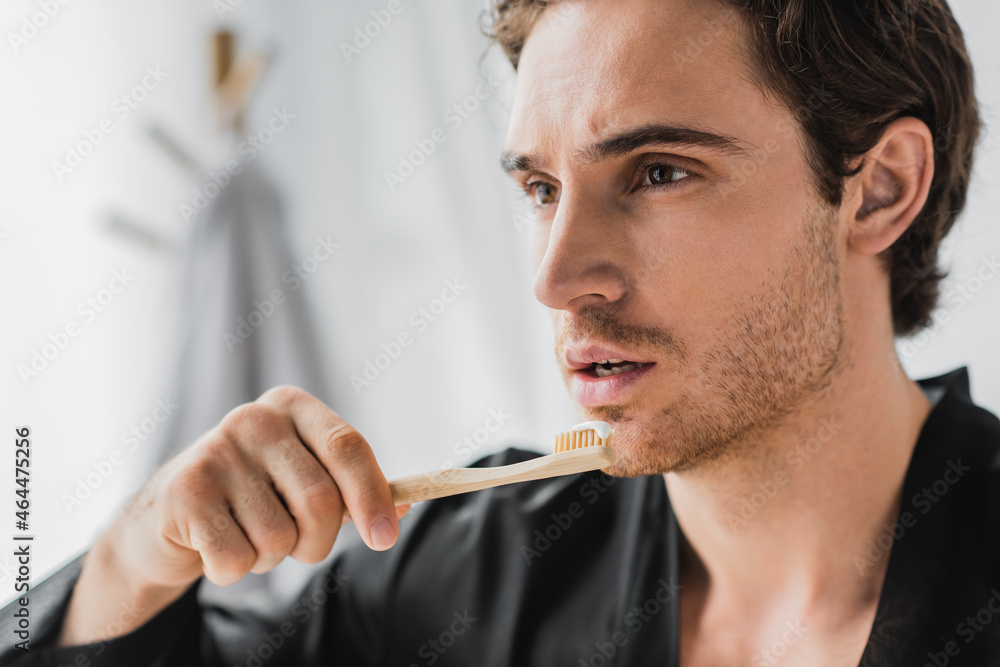 Young man in black robe holding wooden toothbrush with toothpaste in bathroom Young man in black robe holding wooden toothbrush with toothpaste in bathroom