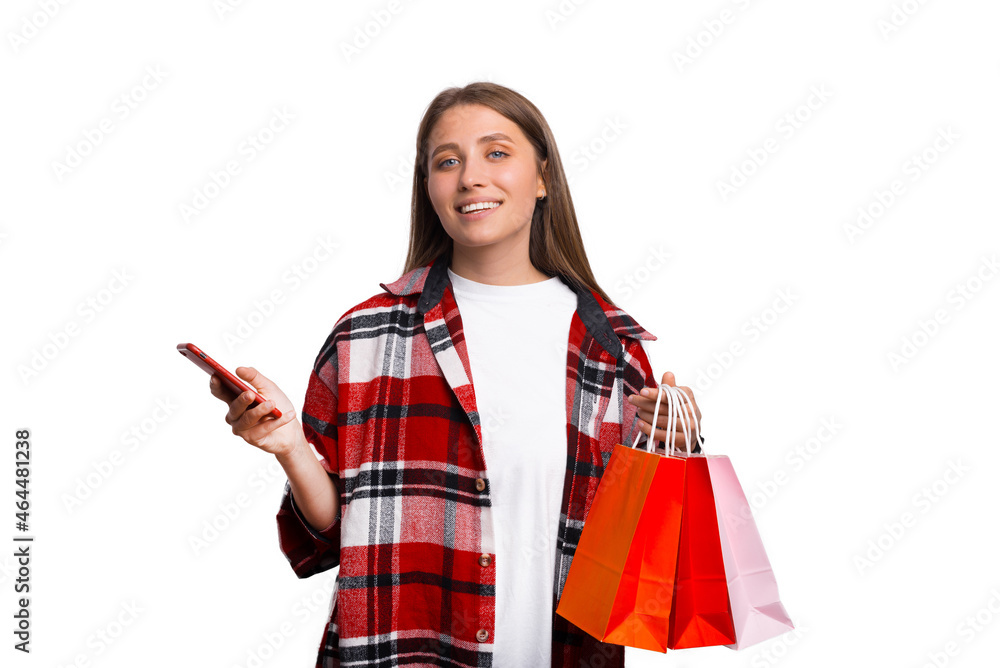 Young woman wearing plaid shirt is holding some shopping bags and her phone. Young woman wearing plaid shirt is holding some shopping bags and her phone.