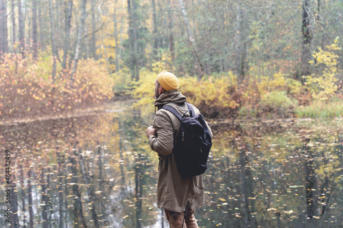 Traveler in the woods. A man with a backpack walks and trips on a track in a beautiful autumn forest and admires the lake and natural views. Traveling to nature in the forest alone