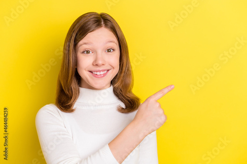 Photo young charming small girl good mood smile point finger empty space isolated on yellow color background