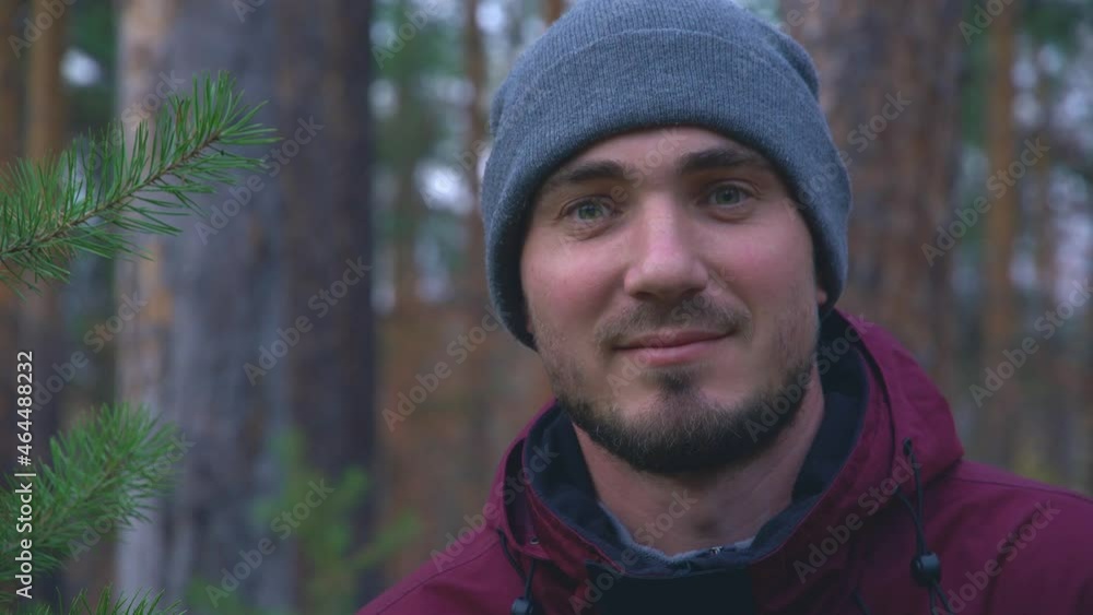 Close-up portrait of a young man in a pine forest who smiles and winks an eye. Contented Traveler in the Forest. Leisure, bio-tourism Close-up portrait of a young man in a pine forest who smiles and winks an eye. Contented Traveler in the Forest. Leisure, bio-tourism
