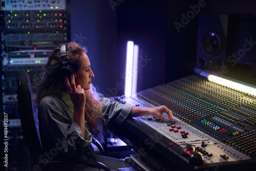Foto Female musical producer in headphones writing music on music keyboard in the stu