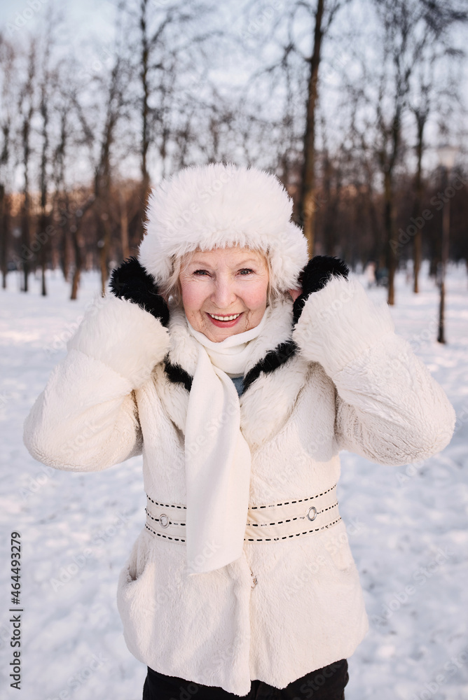 senior woman in white hat and coat jogging in snow winter park. Winter, age, season concept senior woman in white hat and coat jogging in snow winter park. Winter, age, season concept