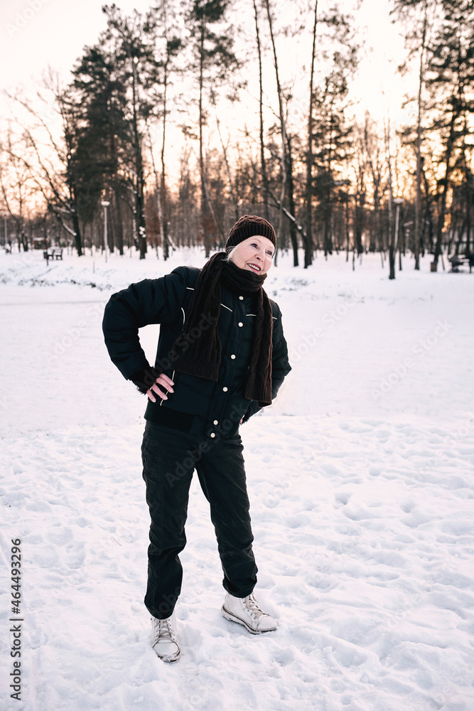 senior woman in hat and sporty jacket doing sports exercises in snow winter park. Winter, age, sport, activity, season concept senior woman in hat and sporty jacket doing sports exercises in snow winter park. Winter, age, sport, activity, season concept