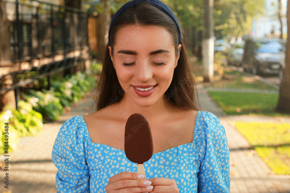 Beautiful young woman holding ice cream glazed in chocolate on city street
