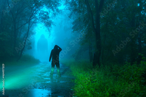 A dark scary concept. Of a man looking at a mysterious bigfoot monster, standing in a forest. At night