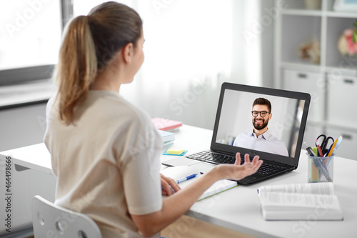education, school and distant learning concept - student woman with laptop computer having video call with man or teacher at home