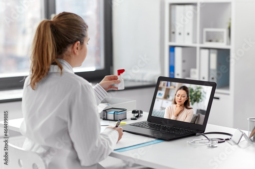 healthcare, technology and medicine concept - female doctor having video call with sick woman patient on laptop computer at hospital and showing oral spray