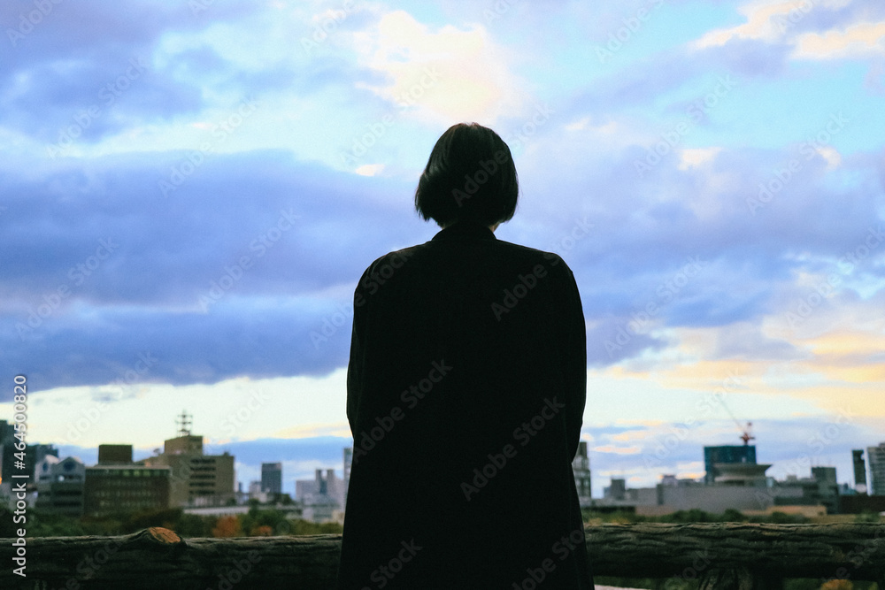 Fototapeta premium 夕方の空と街並みを眺める女性のシルエット