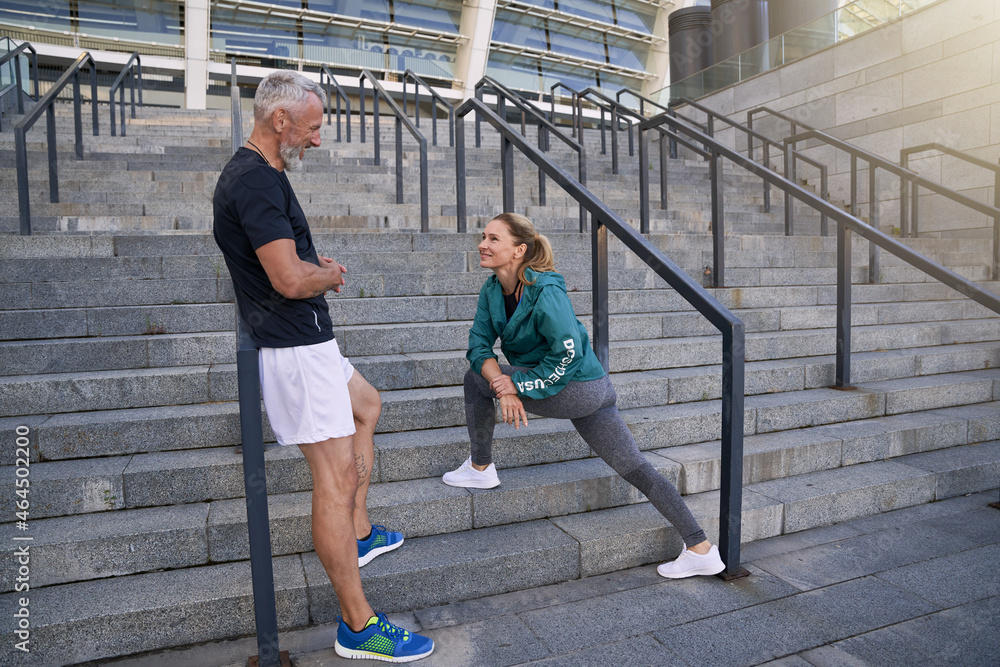 Healthy mature couple chatting while standing outdoors after morning workout in the city