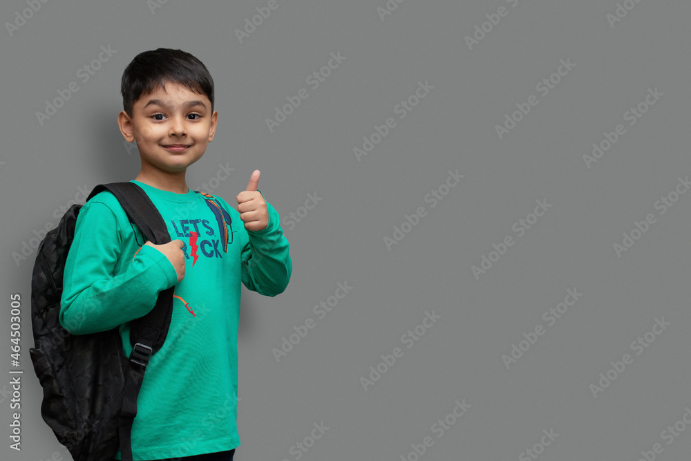 Happy smiling boy with thumb up is going to school. Child with school bag and books. Kid indoors on a background. Back to school.
