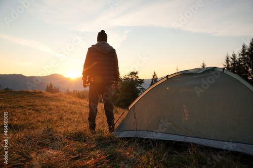 Fotografia Man near camping tent in mountains at sunset, back view