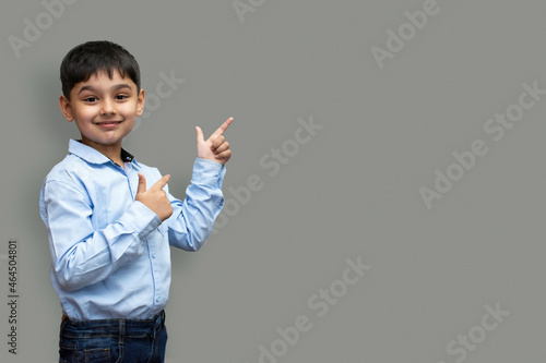 Smiling happy boy pointing finger away at copy space isolated over plain background