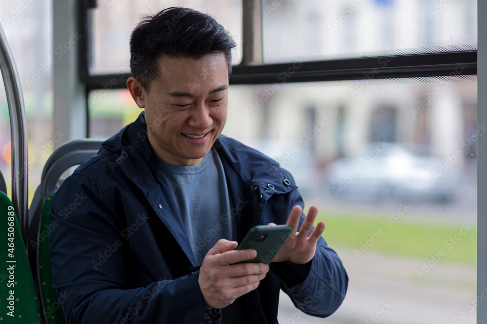 Young asian man corresponds and reads the news online, sitting in the bus, a passenger in casual clothes smiles Young asian man corresponds and reads the news online, sitting in the bus, a passenger in casual clothes smiles