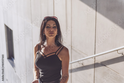 Dark-haired woman posing in a black dress on the concrete stairs. The woman is wearing black sunglasses. It's a beautiful sunny day.