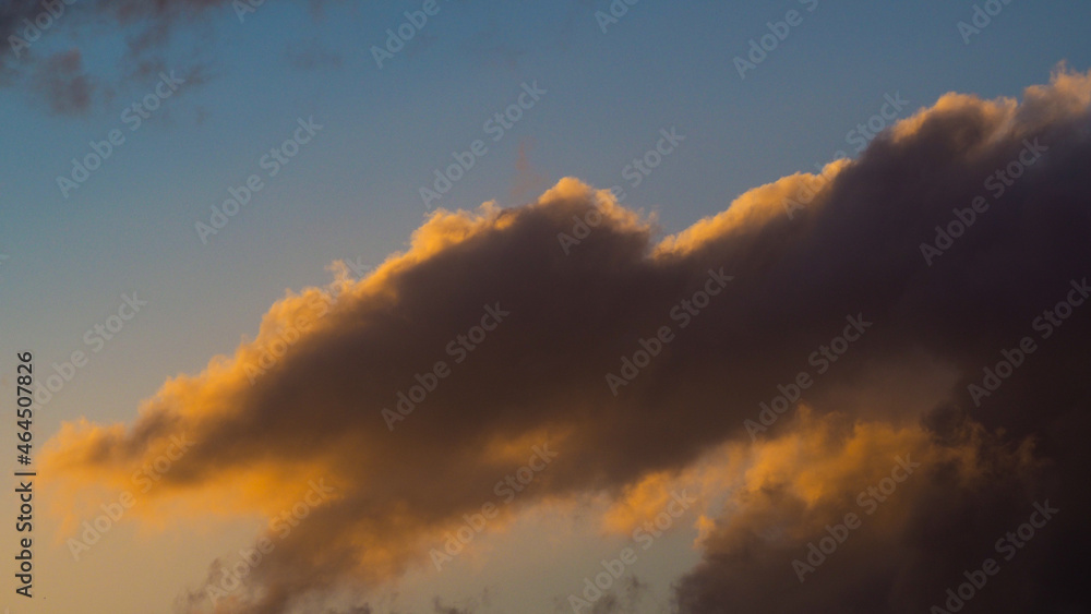 Ciel rougeoyant pendant le coucher du soleil, induisant des teintes orangées sur des cumulus