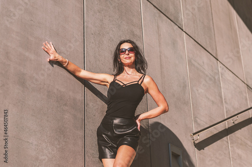 Dark-haired woman posing in a black dress on the concrete stairs. The woman is wearing black sunglasses. It's a beautiful sunny day. © Photoisfundude