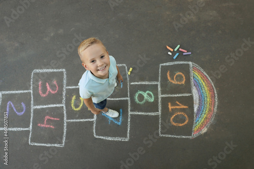 Little boy and colorful hopscotch drawn with chalk on asphalt outdoors, top view. Happy childhood photo
