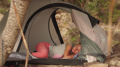 Young brunette long-haired girl sleeps calmly in small camp tent on wild beach under palm trees on gloomy day in Vietnam closeup