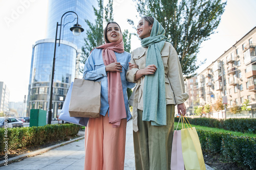 Two female muslim shopaholics walking through the street after great shopping