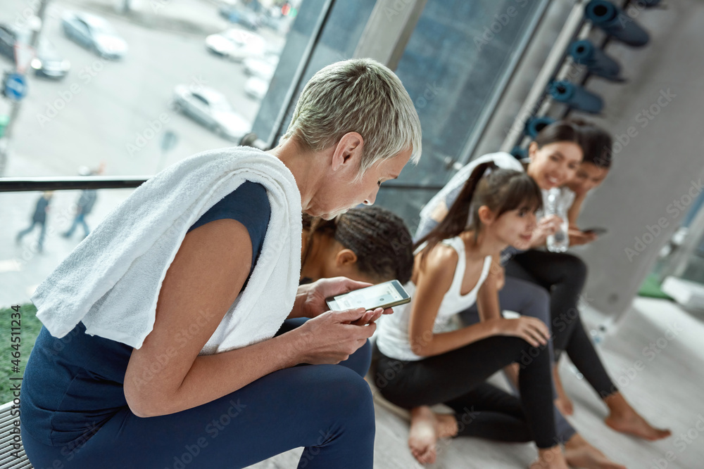 Diverse women relax using devices after workout Diverse women relax using devices after workout