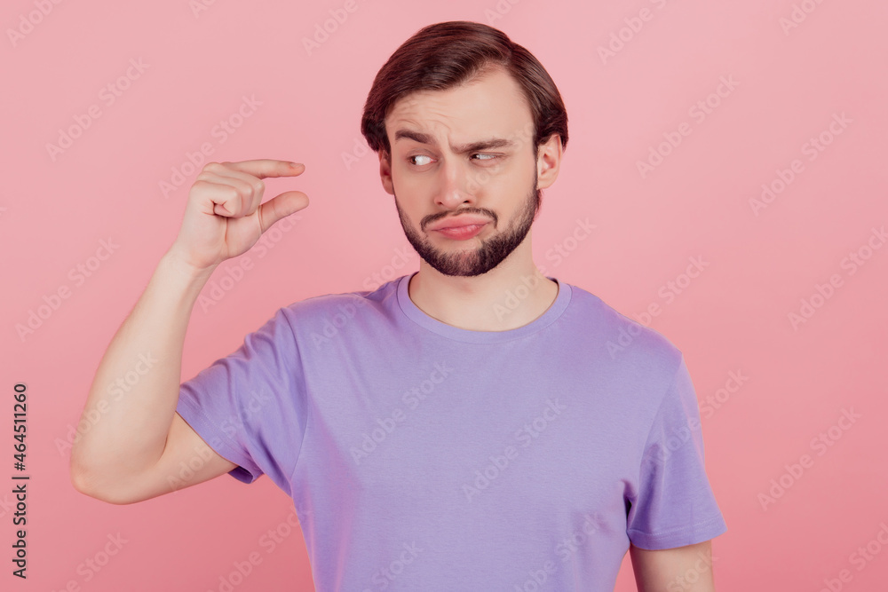 Fototapeta premium Photo of young man unhappy sad upset show tiny small size measures with fingers dislike isolated over pink color background