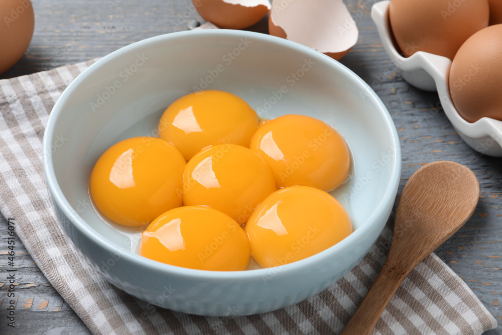 Bowl with raw egg yolks on grey wooden table, closeup