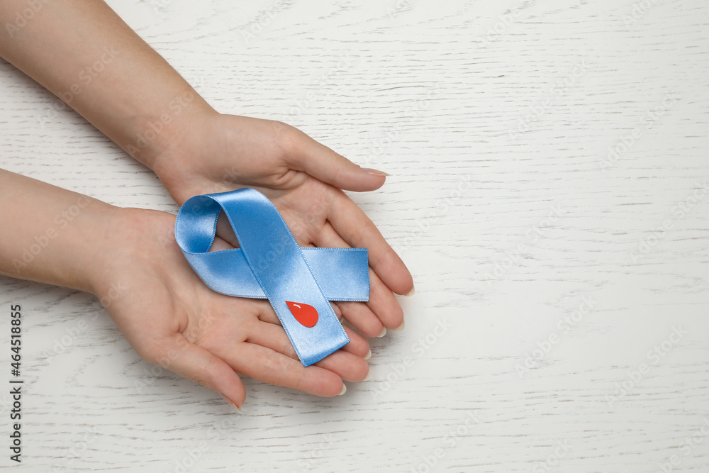 Woman holding light blue ribbon with paper blood drop at wooden table, top view and space for text. Diabetes awareness Woman holding light blue ribbon with paper blood drop at wooden table, top view and space for text. Diabetes awareness
