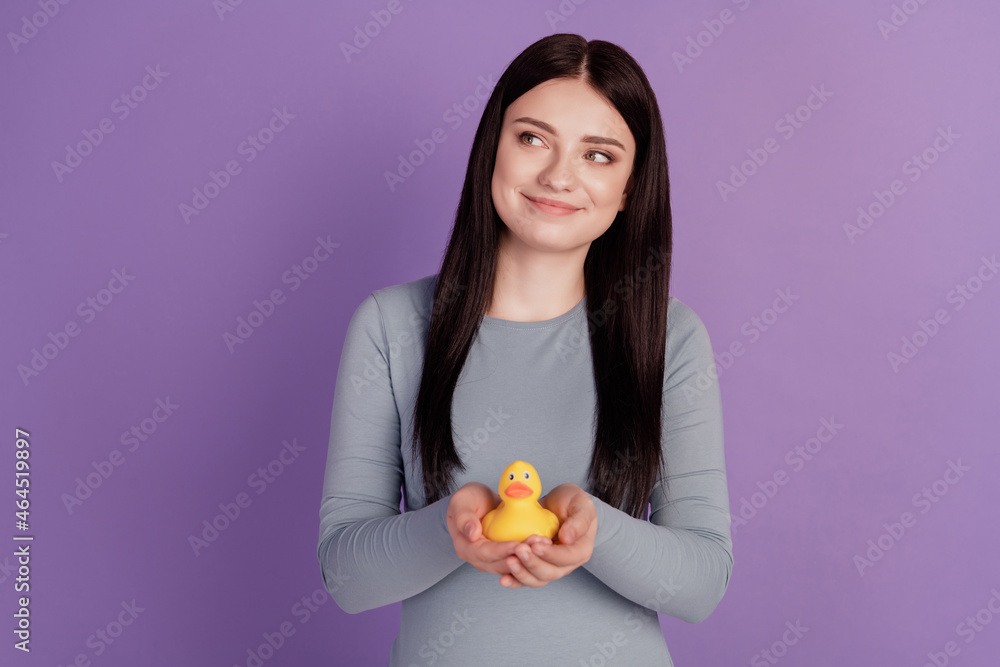 Photo of young lovely girl play rubber duck curious wondered look empty space isolated over purple color background Photo of young lovely girl play rubber duck curious wondered look empty space isolated over purple color background