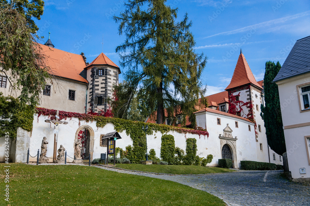 Benesov nad Ploucnici, North Bohemia, Czech Republic, 2 October 2021: old saxoxy renaissance castle at autumn sunny day, graceful towers with spiers, ivy braided white walls, green trees at street