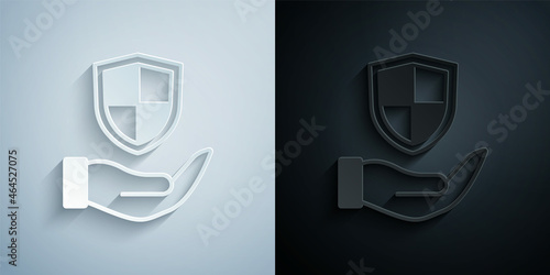 Paper cut Shield in hand icon isolated on grey and black background. Insurance concept. Guard sign. Security, safety, protection, privacy concept. Paper art style. Vector