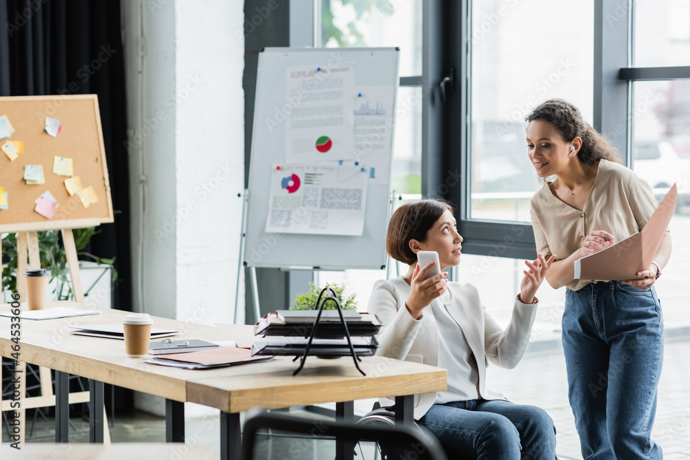 Obraz premium african american businesswoman and her colleague in wheelchair working near blurred flip chart with analytics