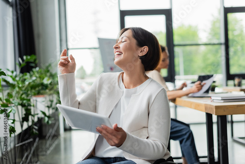 excited businesswoman with physical disability laughing while holding digital tablet in office
