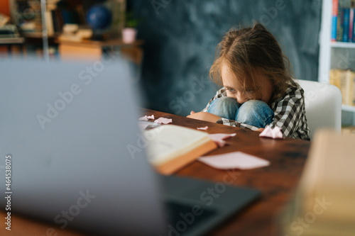 Exhausted upset primary child school girl sitting alone hugging knees in front of desk with difficult homework. Upset angry schoolgirl put head on knee being stressed with homework, selective focus.