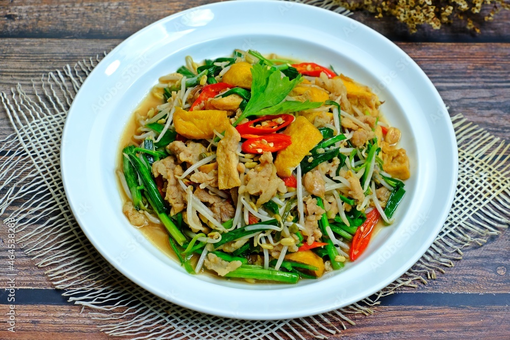 Stir fried tofu with bean sprouts, green chives and minced pork in white plate on wooden table. Stir fried tofu with bean sprouts, green chives and minced pork in white plate on wooden table.
