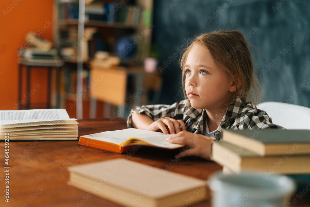 Close-up view of focused pupil school girl kid listening to teacher sitting sitting at table with paper book in classroom. Portrait of elementary child schoolgirl studying at home, selective focus. Close-up view of focused pupil school girl kid listening to teacher sitting sitting at table with paper book in classroom. Portrait of elementary child schoolgirl studying at home, selective focus.