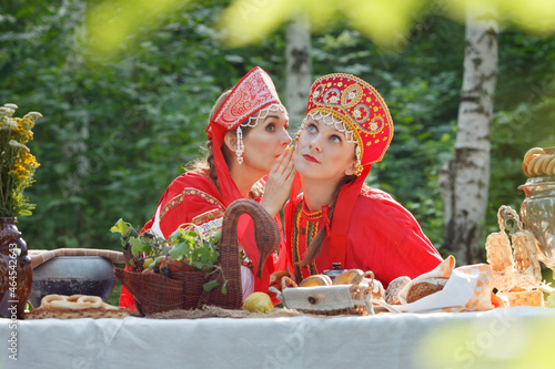 Girl, young russian woman in Russian national sundress, sarafan, and a kokoshnik whispering, emotions, wonder, russian teatime, selective focus photo
