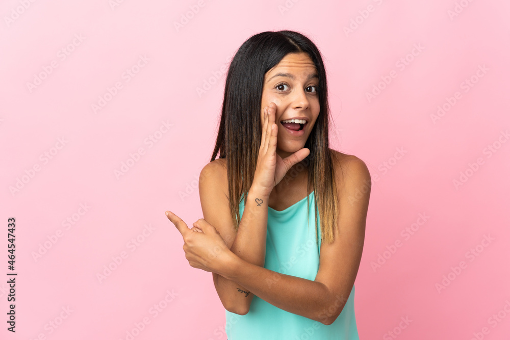 Caucasian girl isolated on pink background pointing to the side to present a product and whispering something Caucasian girl isolated on pink background pointing to the side to present a product and whispering something