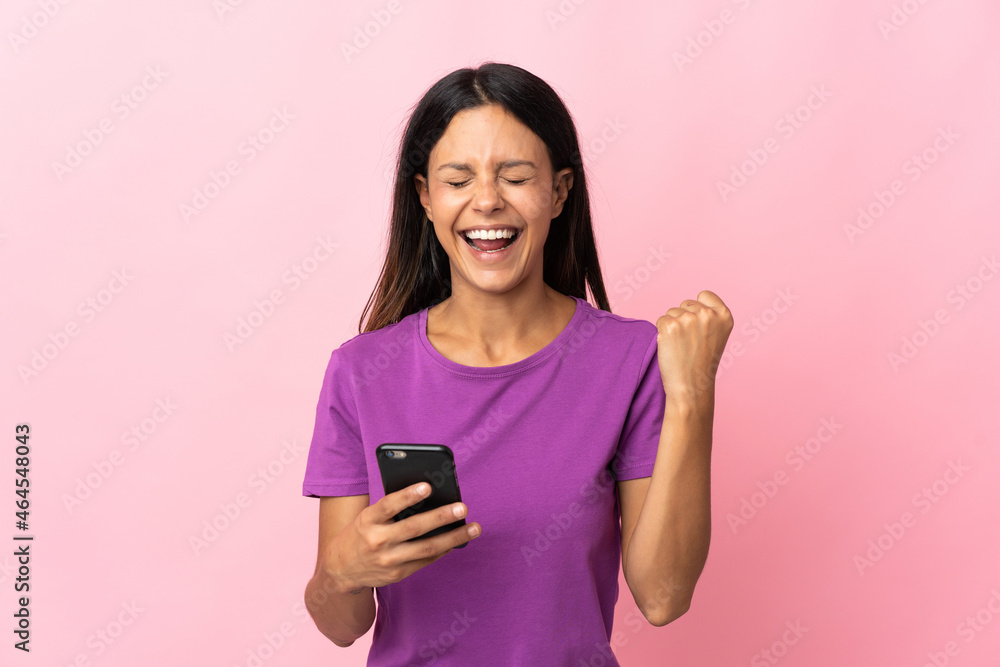 Caucasian girl isolated on pink background using mobile phone and doing victory gesture Caucasian girl isolated on pink background using mobile phone and doing victory gesture